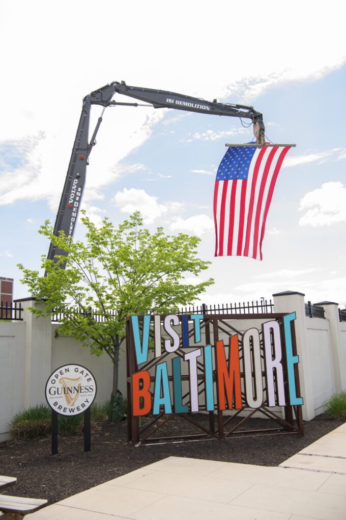 Naiop-USO-@-Guiness-May-2nd-2025-DSC_8480-Copyright-Coyle-Studios-12mgp-680x0-c-default Large American flag hanging from ISI Demolition high reach excavator above Visit Baltimore and Guinness signs