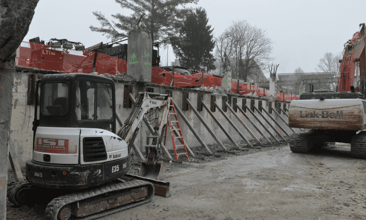 Bobcat and excavator working together near shoring equipment